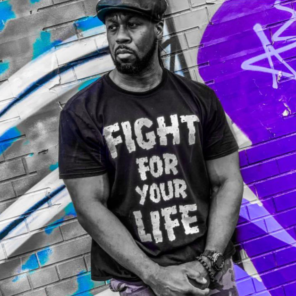 African American male Markane Alan standing against a wall with a printed t-shirt "Fight for your life"